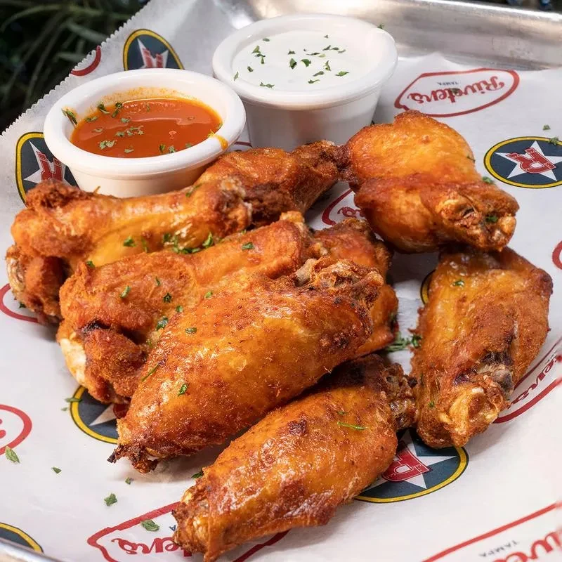 Crispy golden fried chicken wings with two sauces on a Riveters tray.