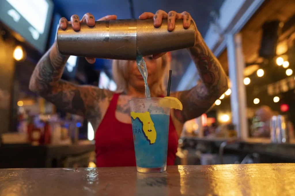Tattooed bartender pours blue drink into a Florida golf glass.