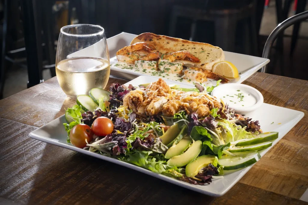 Chicken salad with sauce, wine, and grilled shrimp on wooden table.