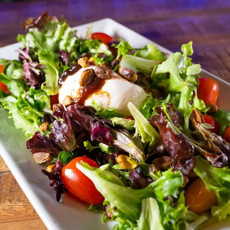 Fresh salad with burrata, tomatoes, greens, balsamic glaze, and pistachios.