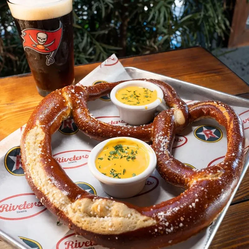 Soft pretzel, cheese dip, and beer with Tampa Bay Buccaneers logo.