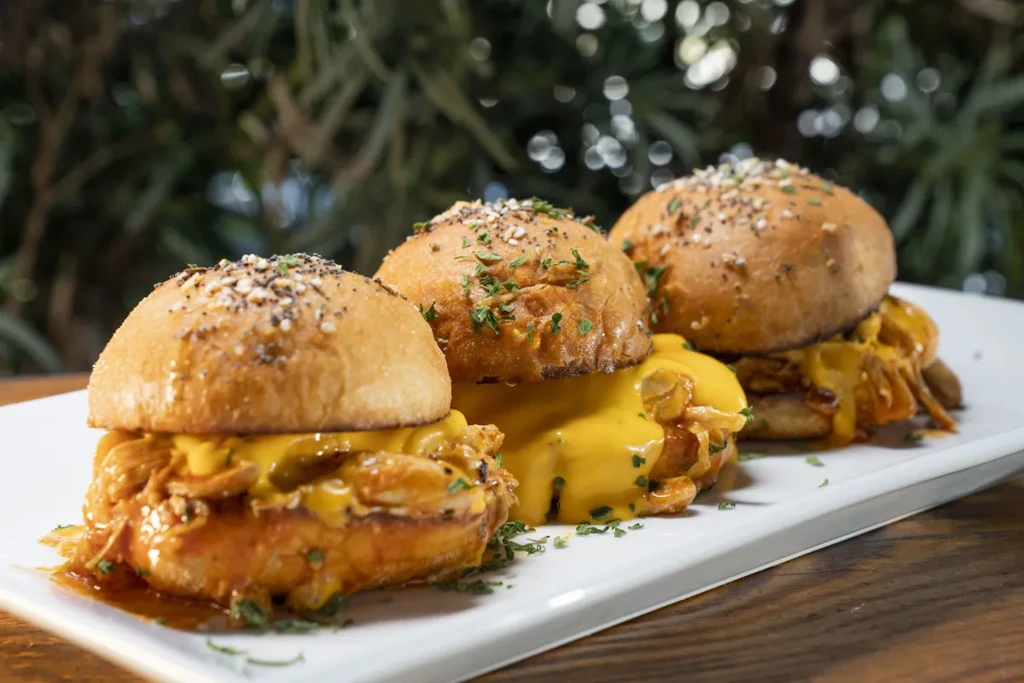 Three pulled meat sliders with cheese sauce and dark sauce.