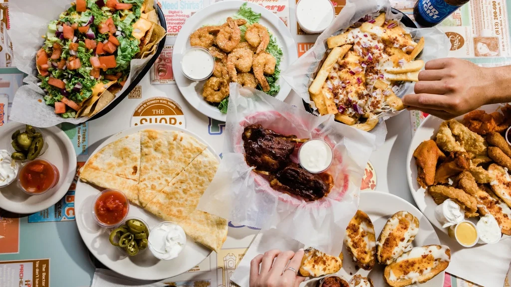 Overhead of nachos, fries, shrimp, ribs, and beer with hands.