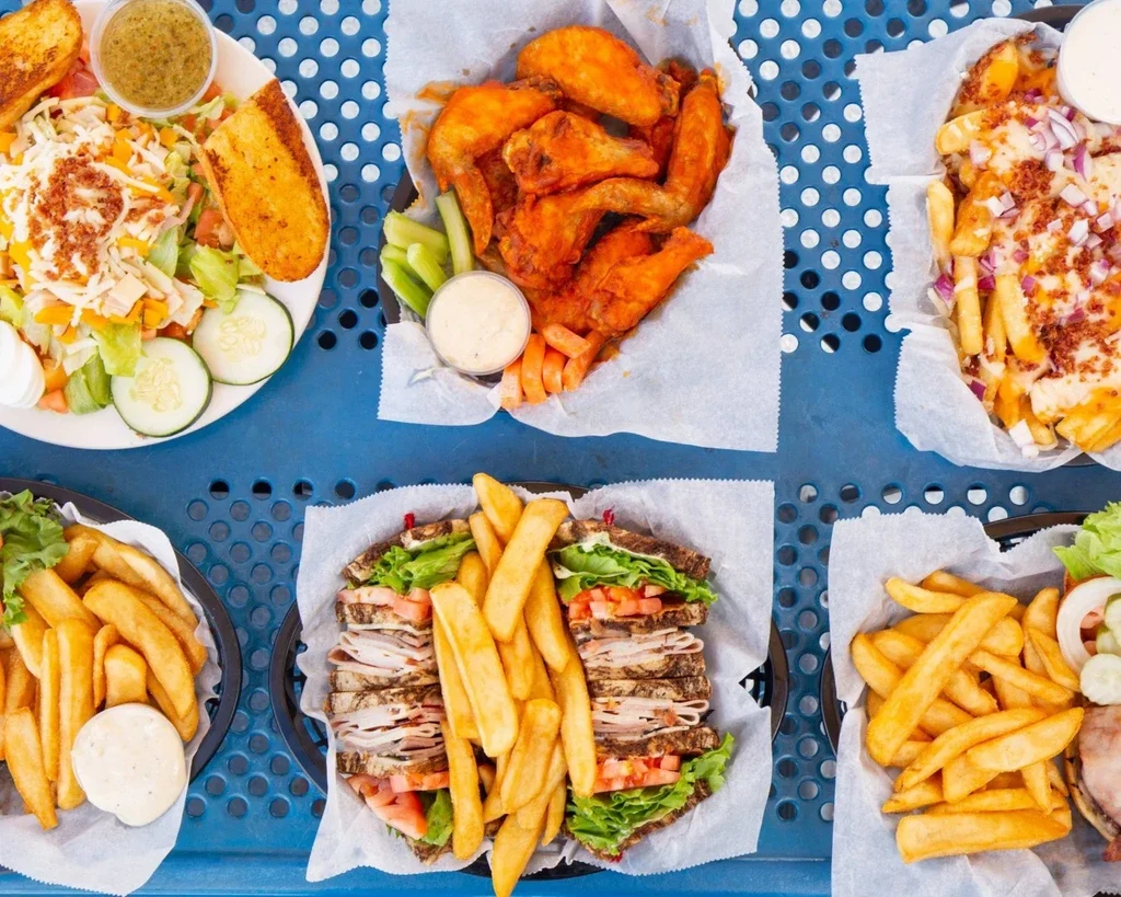 Flat lay with salad, wings, fries, and sandwiches on blue table.
