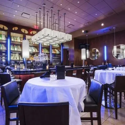 Modern restaurant interior with an elegant table, illuminated bar, and chandelier.