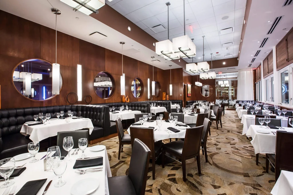 Empty, elegant restaurant dining room with set tables and leather booths.
