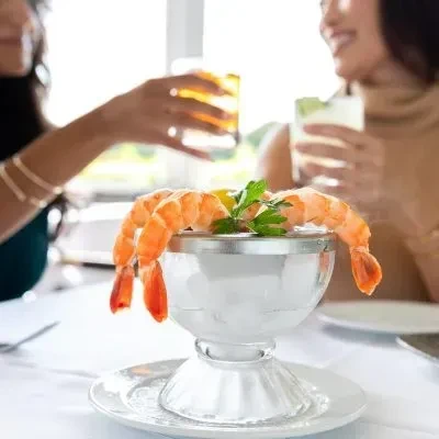 Large shrimp cocktail in a clear glass bowl with lemon and parsley.