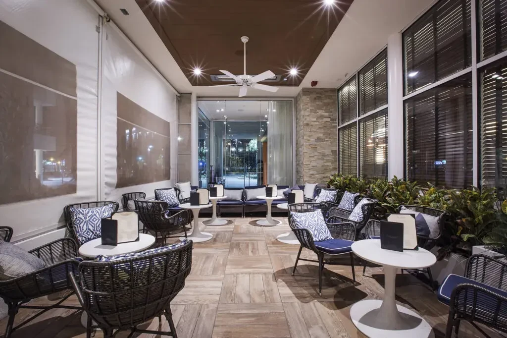 Empty modern lounge with blue chairs, white tables, and warm lighting.