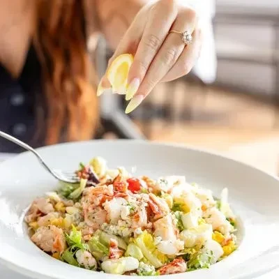 A hand squeezes lemon over a seafood salad in a white bowl.