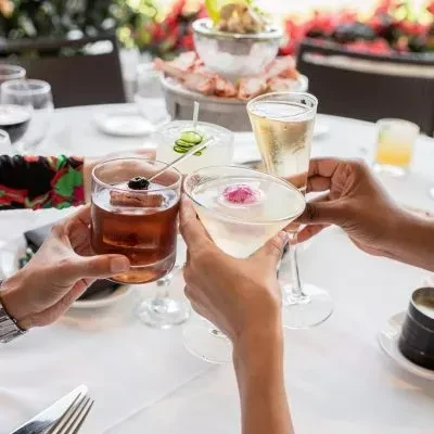 Hands clinking four unique cocktails in an upscale restaurant toast.