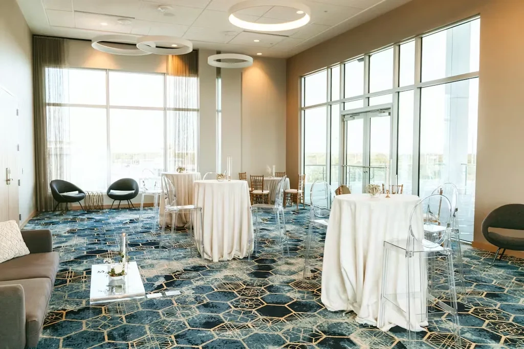 Modern event space with blue-gold carpet, high-top tables, and large windows.
