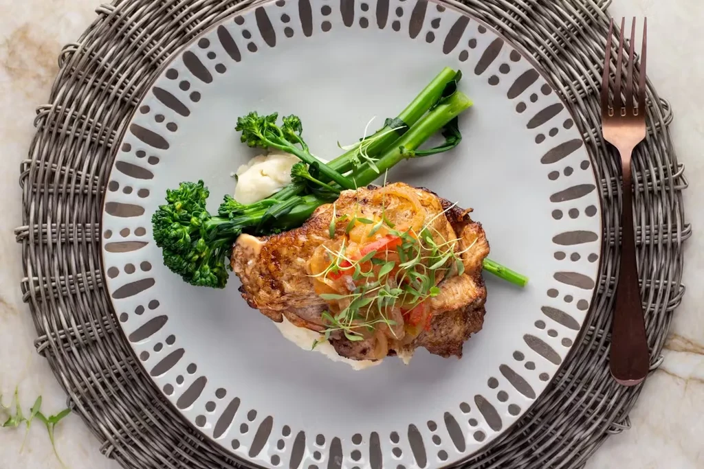 Elegant plated seared meat, potatoes, broccolini, onions, peppers, microgreens.