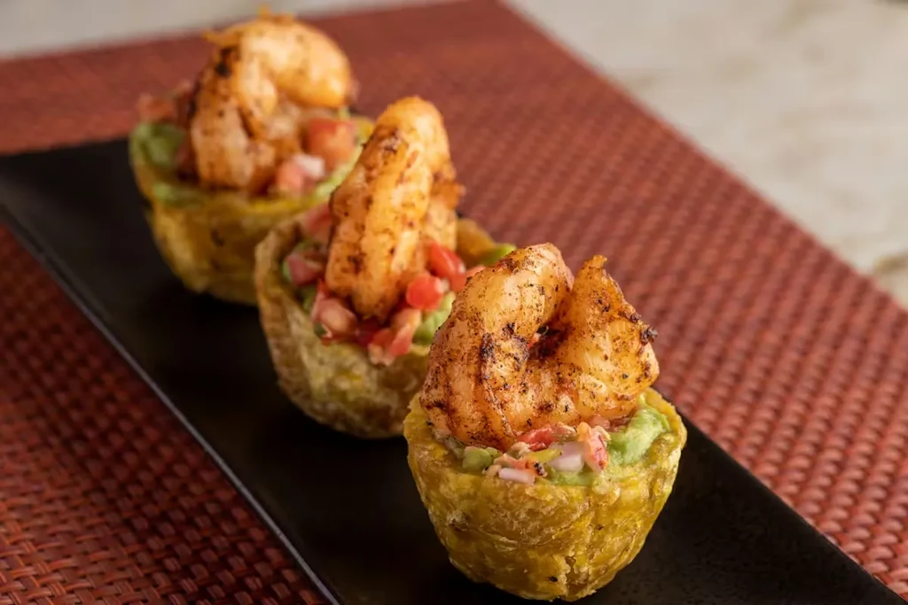 Three grilled shrimp on tostones cups with guacamole and tomatoes.