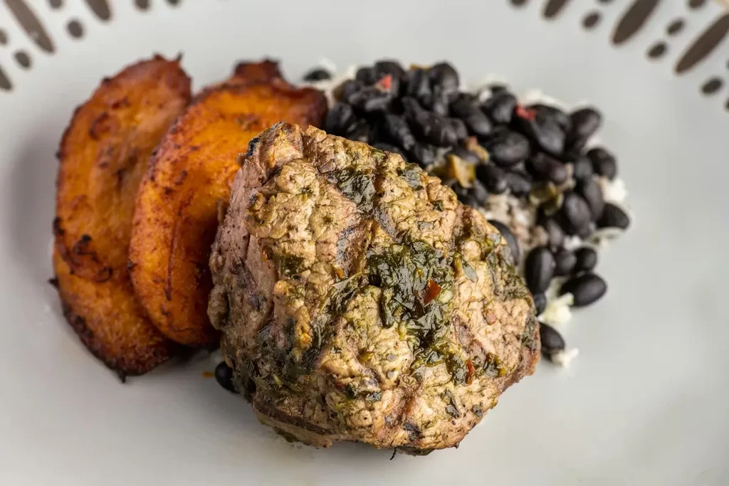 Plated meal: green-sauced meat, plantains, and rice with black beans.
