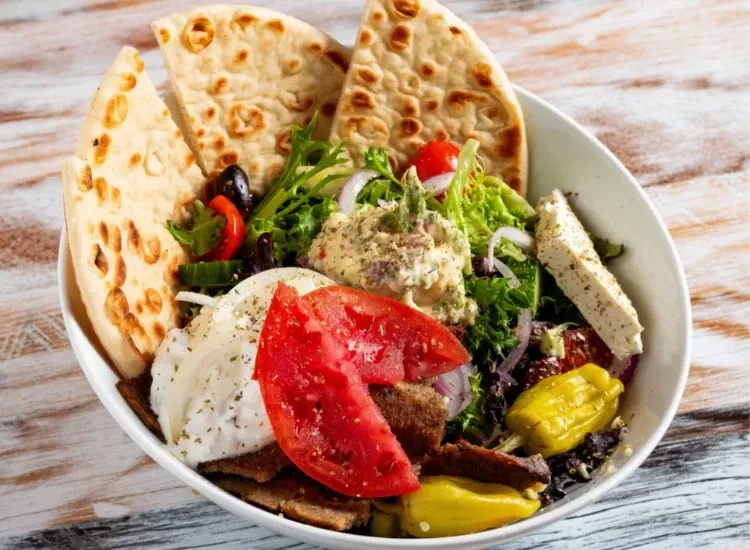 Greek gyro platter with pita, meat, vegetables, tzatziki, hummus, and feta.