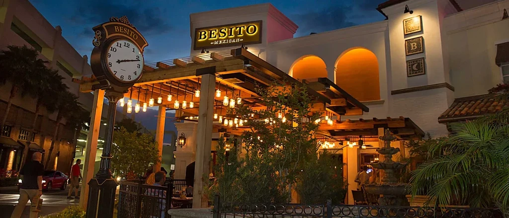 Well-lit Besito Mexican restaurant facade, patio, and ornate clock at night.