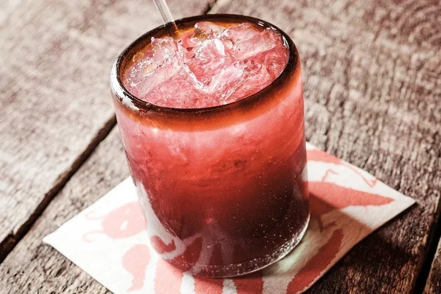 Close-up of vibrant red iced drink with straw on lobster coaster.