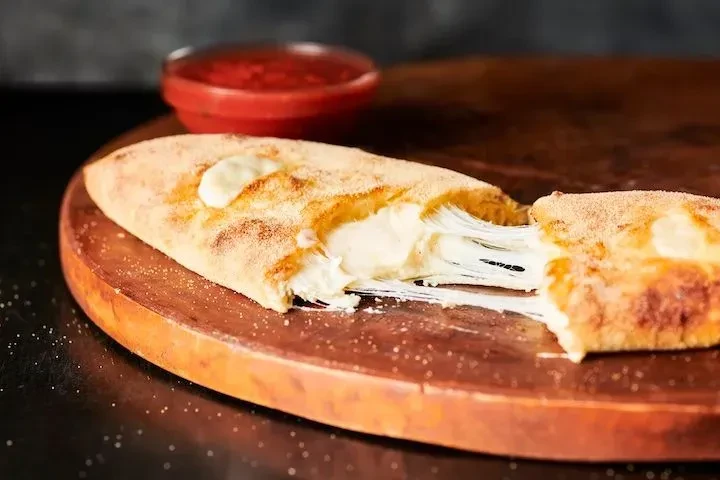 Golden-brown calzone cut open, stringy melted cheese, red sauce.