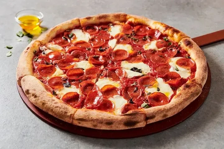 Freshly baked pepperoni pizza with mozzarella and herbs on a peel.