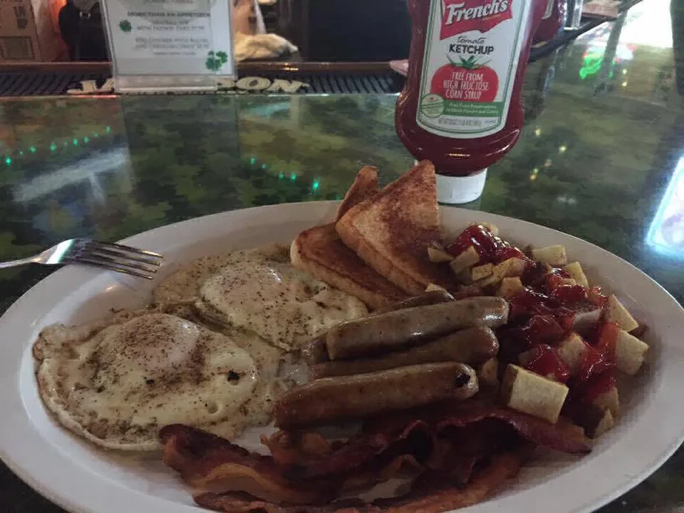 Breakfast plate with eggs, bacon, sausage, home fries, and toast on bar.