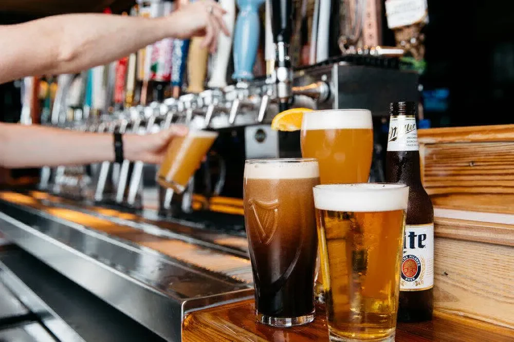 Guinness, lager, and Miller Lite on bar with person pouring beer.