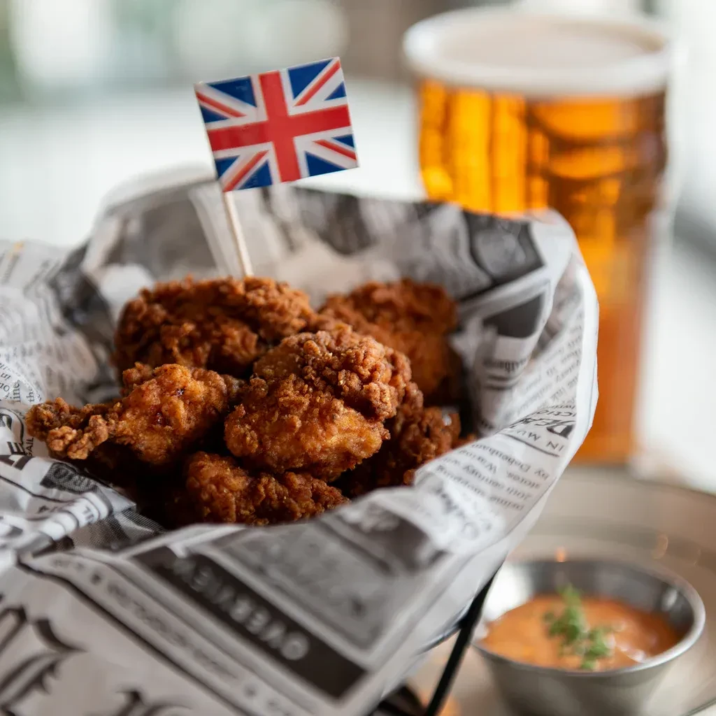 Close-up of fried chicken, Union Jack flag, beer, and dipping sauce.