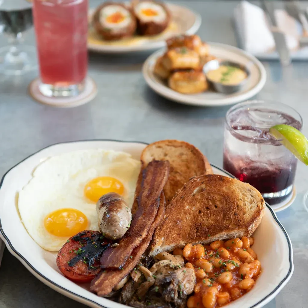 Hearty English breakfast with fried eggs, bacon, sausage, beans, and toast.