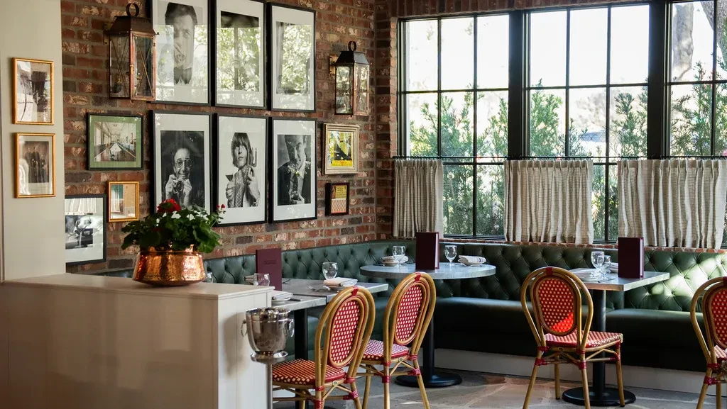 Restaurant interior with brick wall, framed art, green booth, and windows.