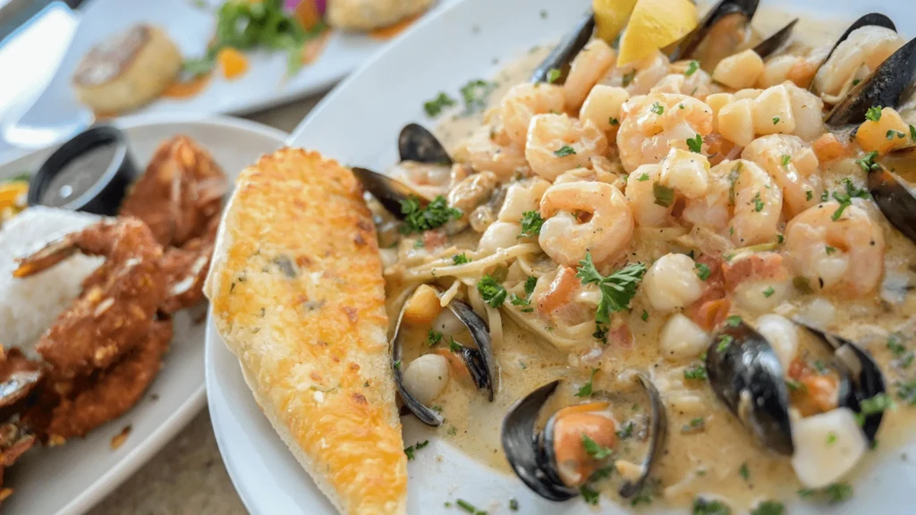 Close-up of creamy seafood pasta, garlic bread, and blurred dishes.