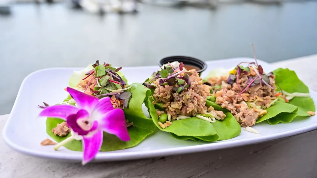 Three lettuce wraps with chopped filling, microgreens, and orchid.