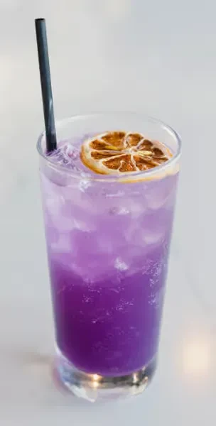 Vibrant purple drink in a glass with ice, straw, and dried citrus slice.