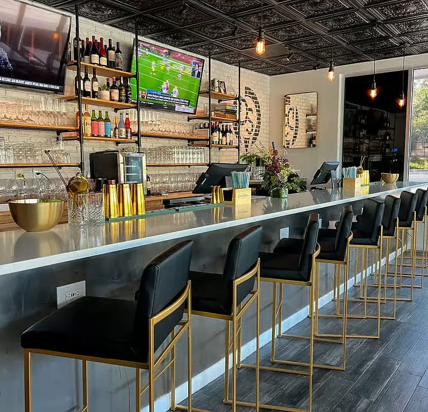 Modern restaurant bar with sleek counter, gold stools, and shelved bottles.