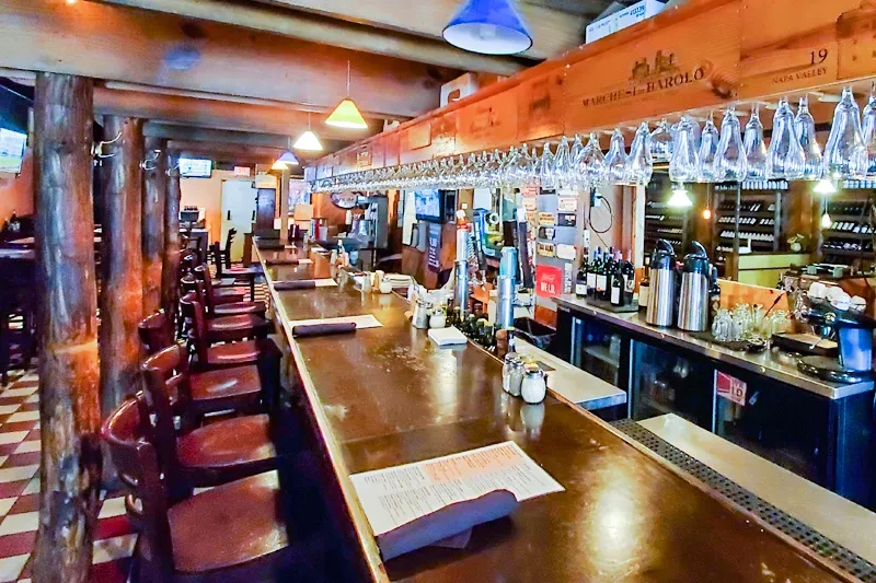 Empty rustic bar interior with long wooden counter and stools.