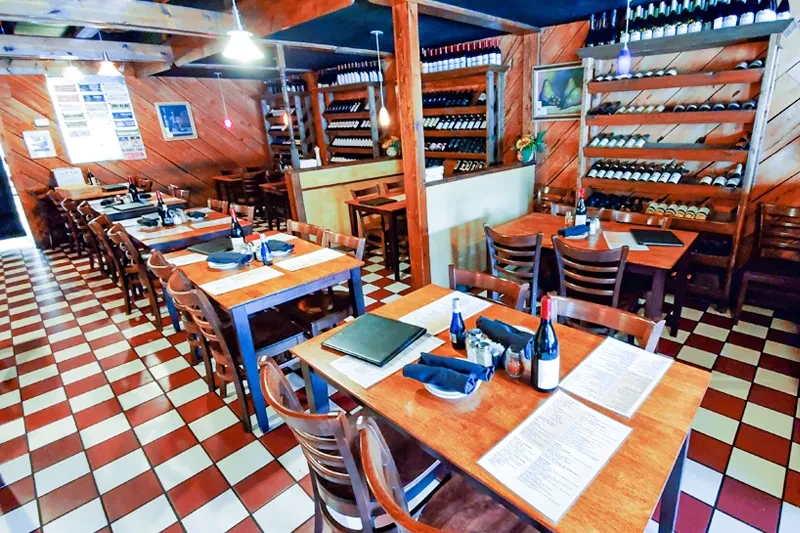 Empty rustic restaurant with wooden tables, wine racks, and checkered floor.