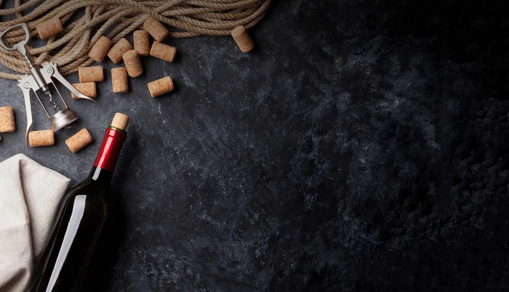Top-down: Wine bottle, corks, corkscrew, rope on dark stone surface.