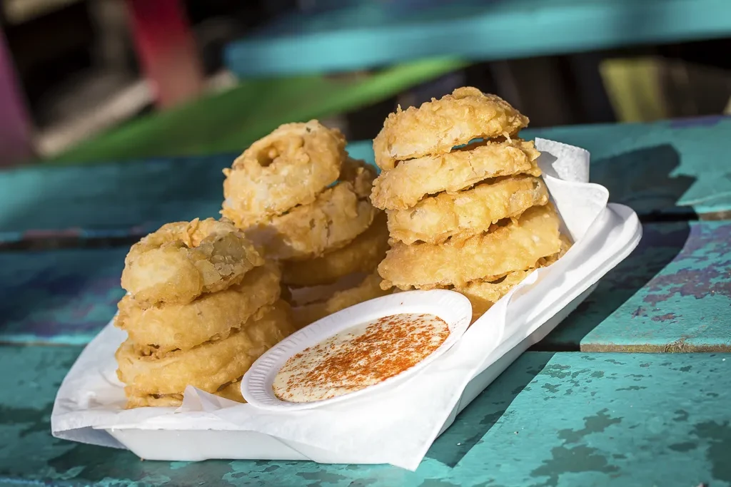 Golden-brown onion rings with creamy sauce on a rustic turquoise table.
