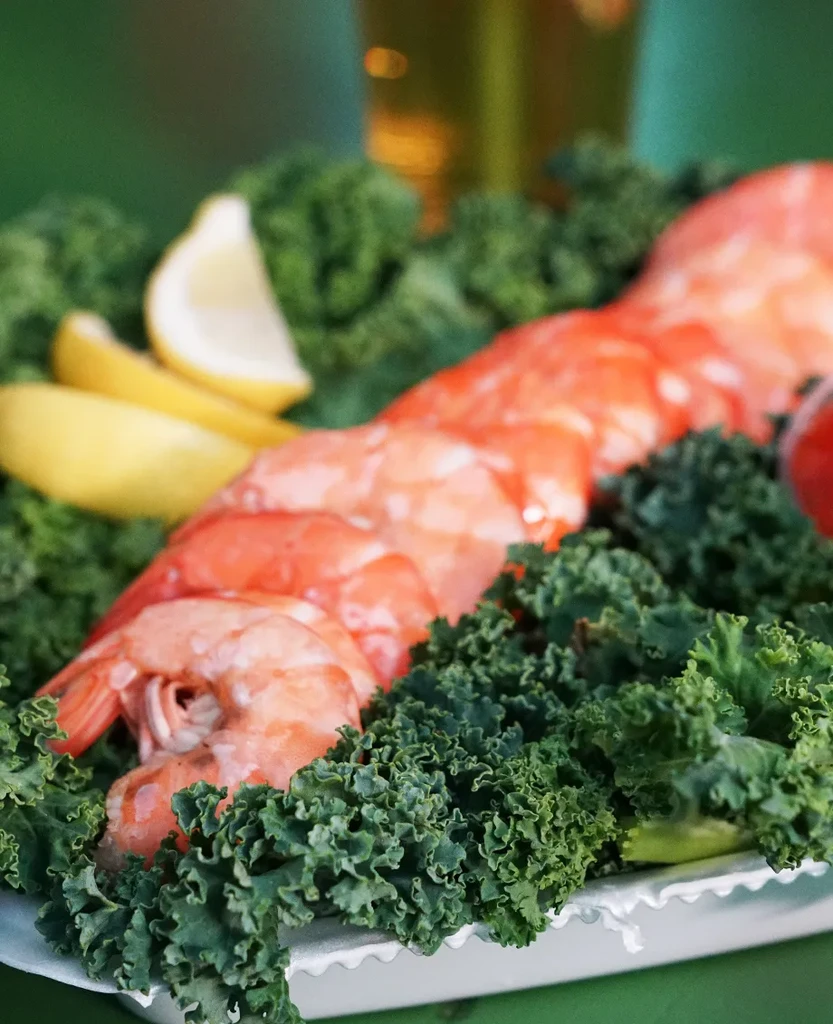 Plate of cooked shrimp and kale with two lemon wedges.