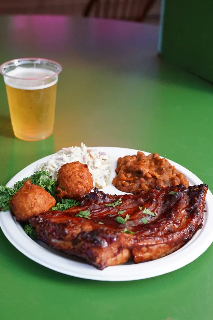Top-down view of barbecued ribs, coleslaw, baked beans, and hushpuppies.