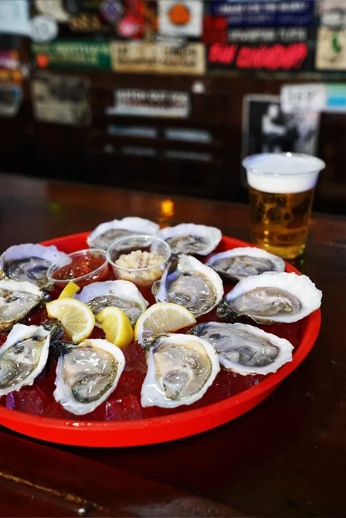 Shucked oysters on ice with lemon, sauces, and a beer.