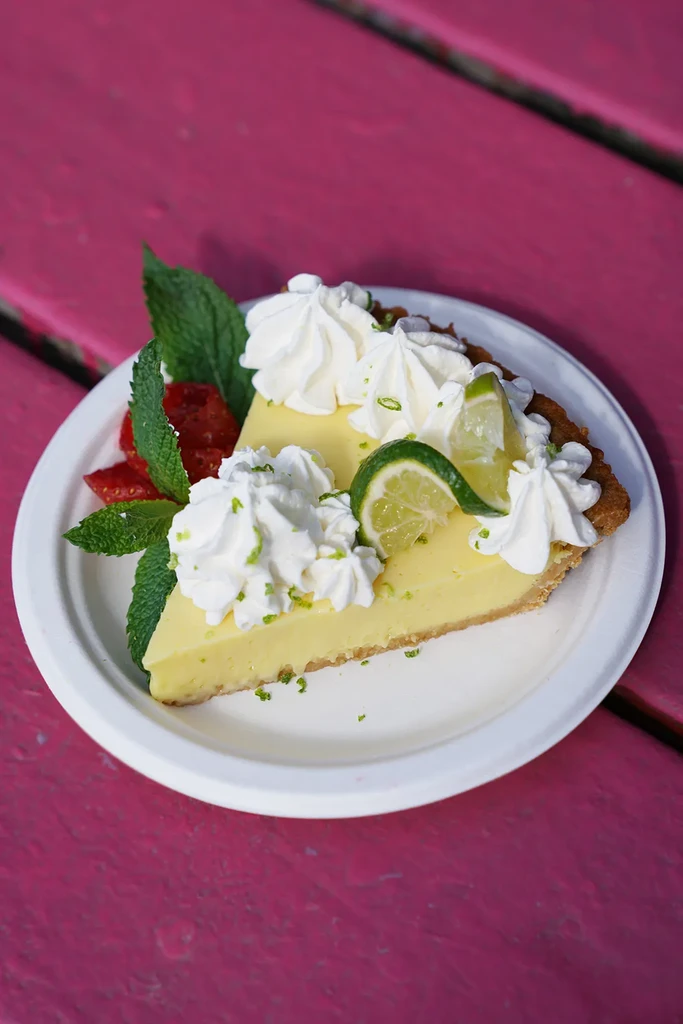 Key lime pie slice with whipped cream, lime, mint, fruit on fuchsia wood.