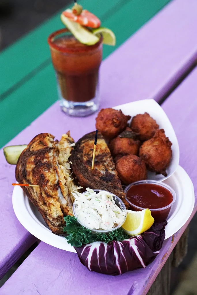 Grilled sandwich meal with sides, Bloody Mary, on colorful picnic table.