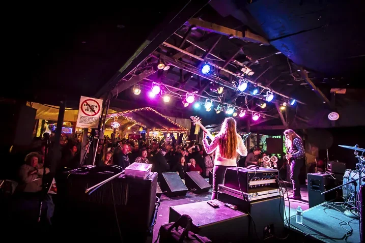 Musicians on stage from behind, facing an audience under colorful lights.