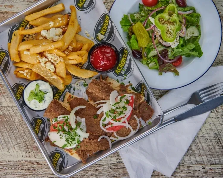 Gyro plate with feta fries, Greek salad on rustic table.