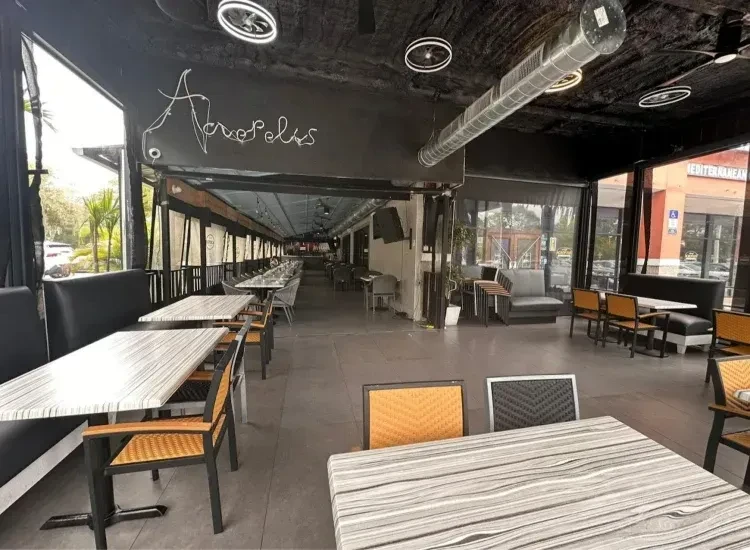 Modern empty restaurant with 'Acropolis' sign, industrial ceiling, and street view.