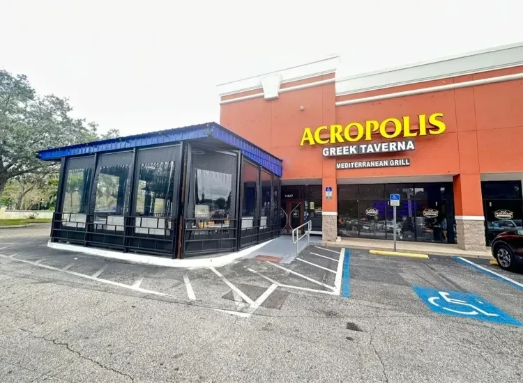 Restaurant exterior: Acropolis Greek Taverna, orange facade, blue-roofed patio, parking lot.