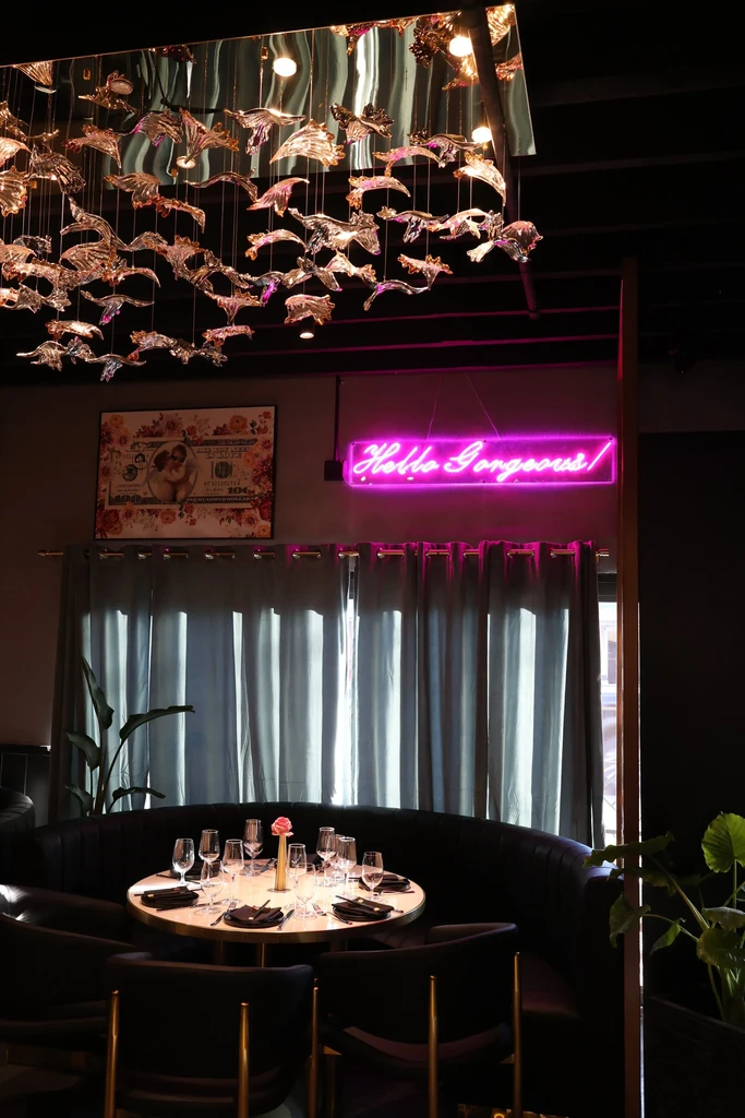 Elegant restaurant interior featuring a circular booth, set table, chandelier, and neon sign.