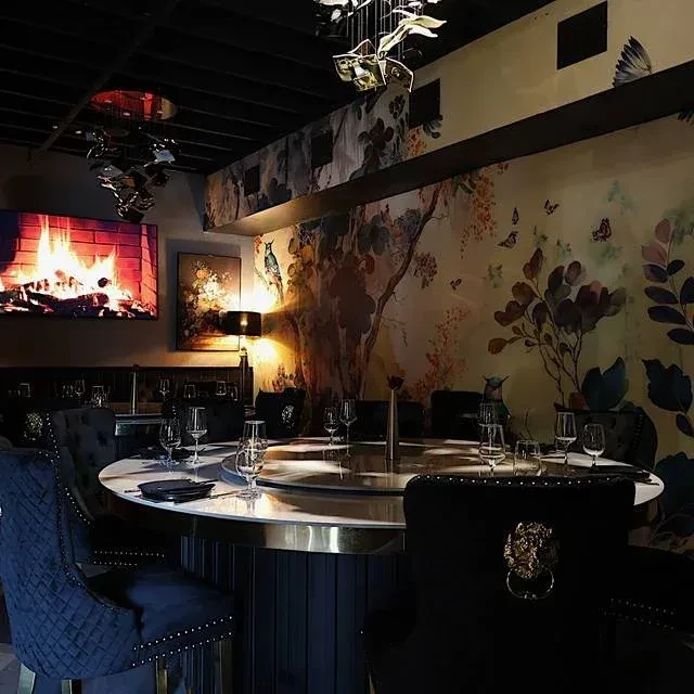 Elegant restaurant interior with a round table, elaborate mural, and digital fireplace.