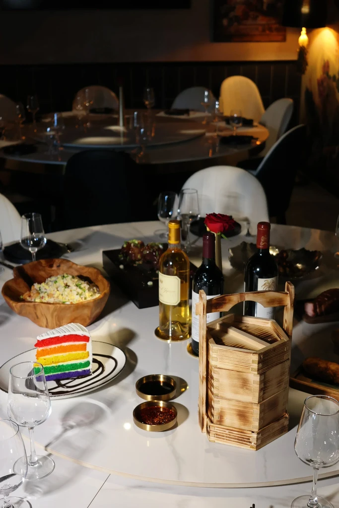 Upscale restaurant table with rainbow cake, wine bottles, and various dishes.