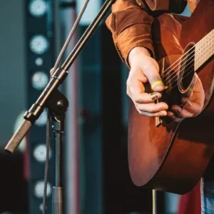 Hands playing an acoustic guitar on stage with warm lighting.