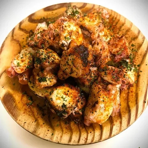 Cooked octopus pieces with paprika and herbs on a wooden plate.